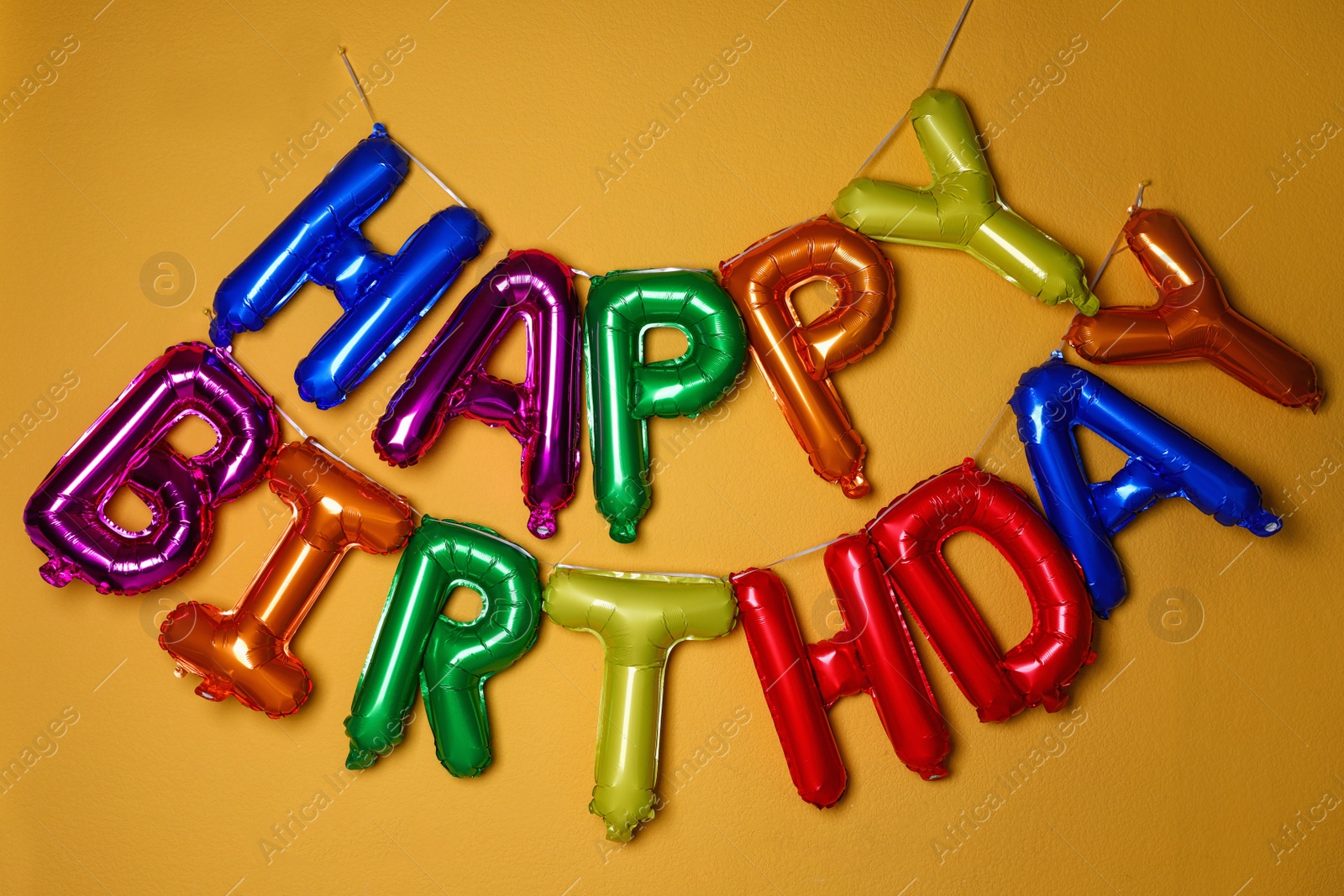 Photo of Phrase HAPPY BIRTHDAY made of colorful balloon letters on orange background