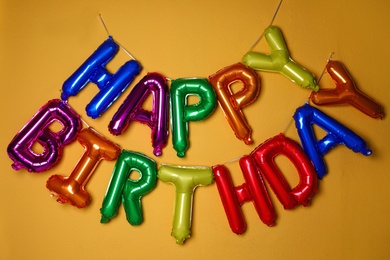 Photo of Phrase HAPPY BIRTHDAY made of colorful balloon letters on orange background