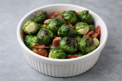 Delicious roasted Brussels sprouts and bacon in bowl on grey table, closeup