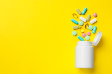 Photo of Different vitamin pills and bottle on yellow background, top view. Space for text