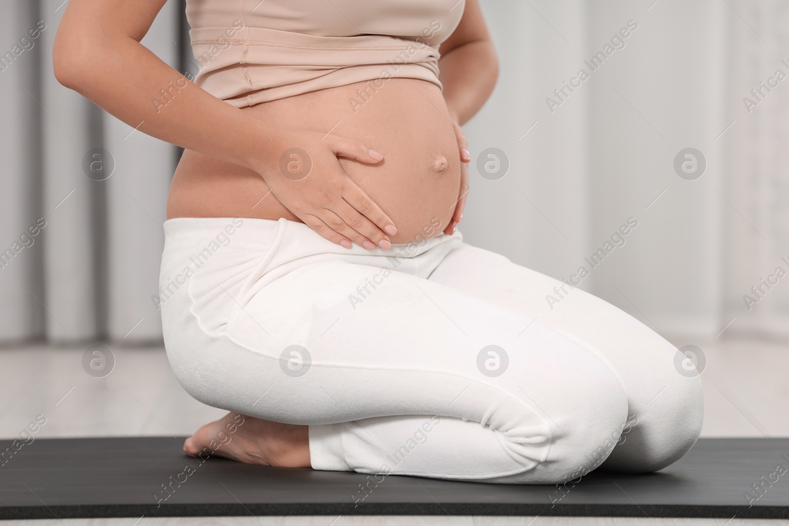 Photo of Pregnant woman sitting on yoga mat at home, closeup