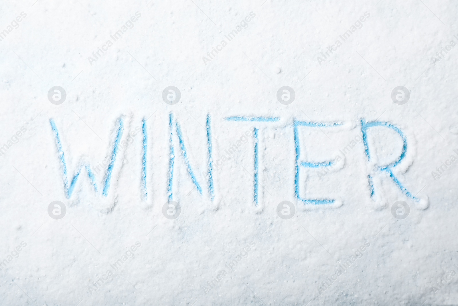 Photo of Word WINTER written in snow on color background, top view