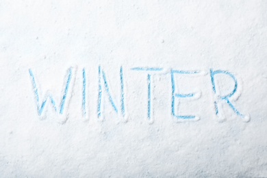 Photo of Word WINTER written in snow on color background, top view