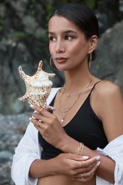 Photo of Beautiful young woman in stylish bikini holding seashell outdoors