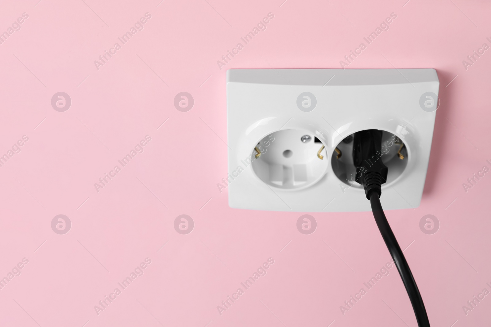 Photo of Power sockets with inserted plug on pink wall, space for text. Electrical supply