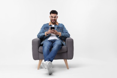 Handsome man using smartphone in armchair on white background