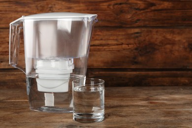 Photo of Filter jug and glass with purified water on wooden table. Space for text