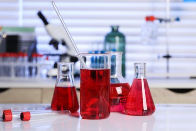 Photo of Laboratory analysis. Different glassware with red liquid on white table indoors