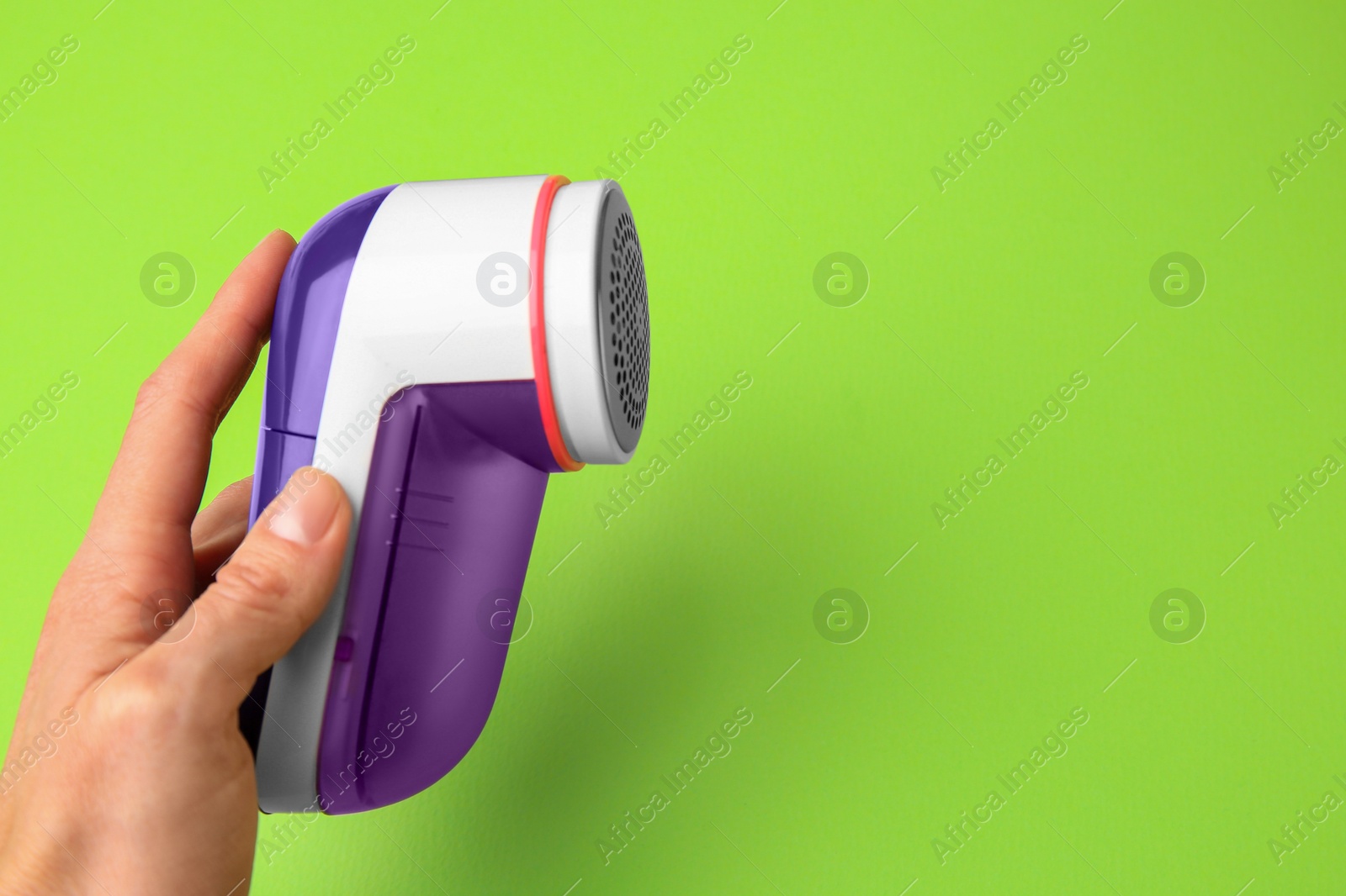 Photo of Woman holding modern fabric shaver on light green background, closeup. Space for text