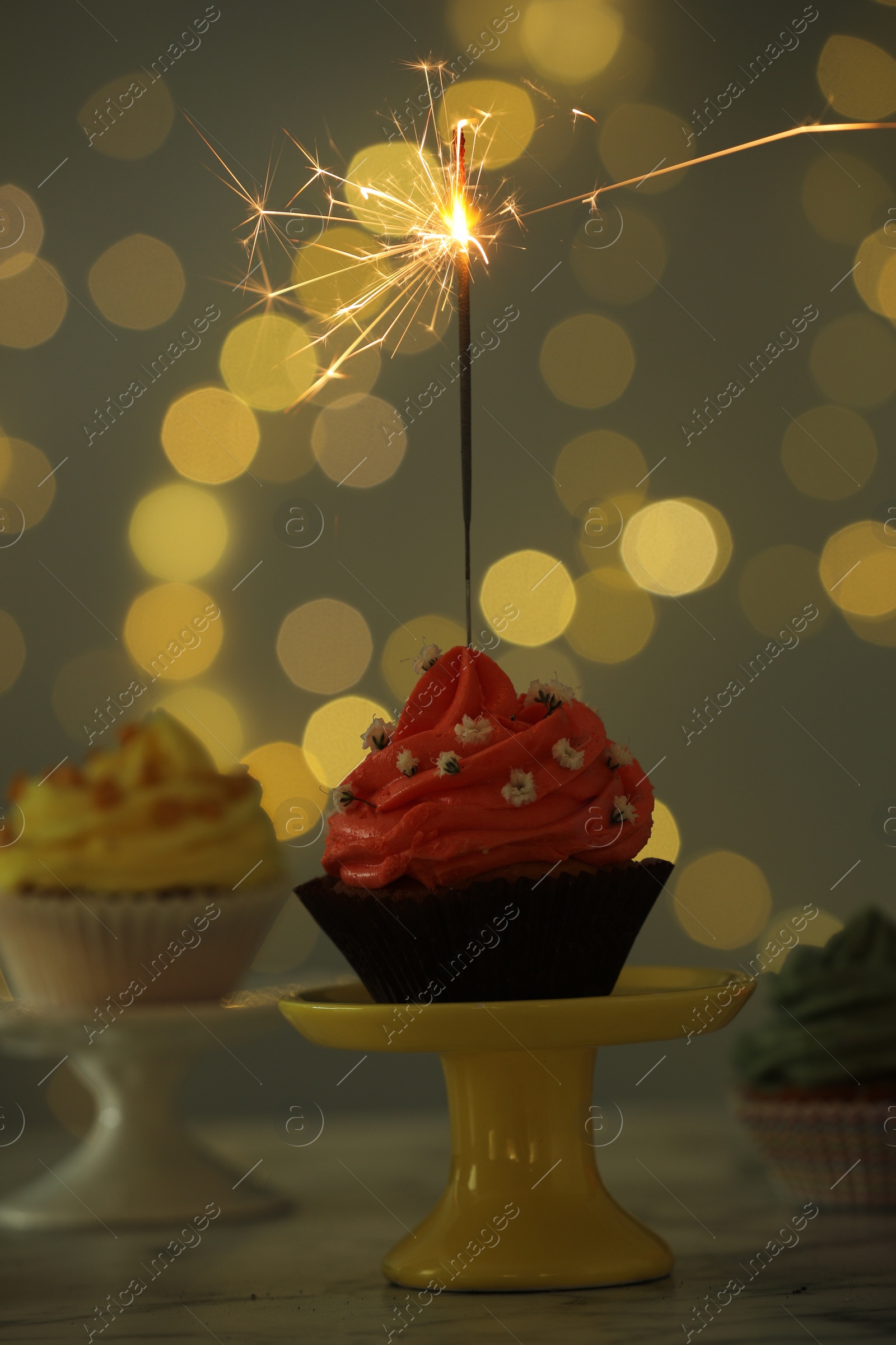 Photo of Delicious cupcake with sparkler on table against blurred lights