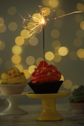 Photo of Delicious cupcake with sparkler on table against blurred lights