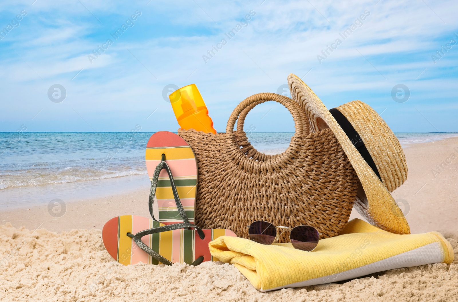 Image of Stylish bag with different accessories on sandy beach near ocean