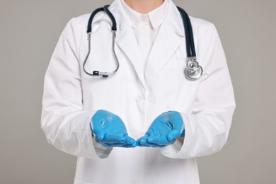 Doctor with stethoscope holding something on grey background, closeup