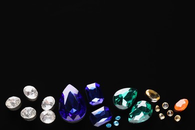 Different beautiful gemstones for jewelry on black background, flat lay. Space for text