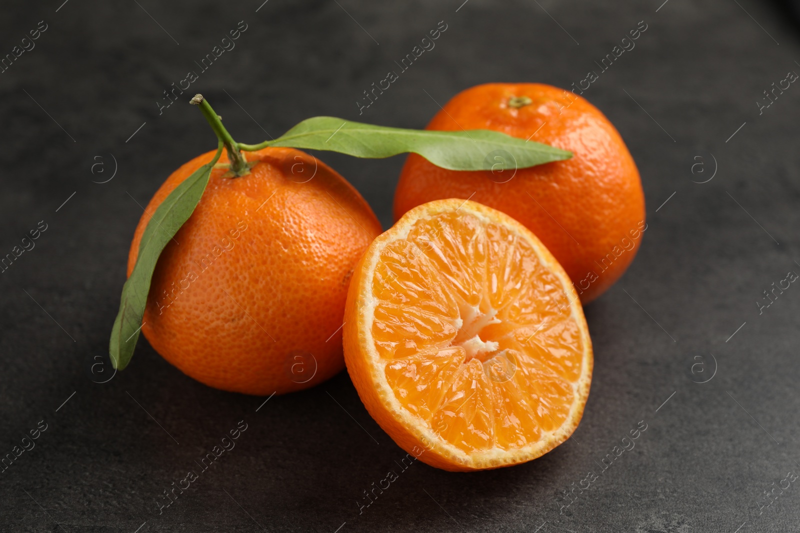 Photo of Fresh ripe tangerines and green leaves on grey table, closeup