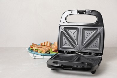 Photo of Modern grill maker and sandwiches on white table, space for text