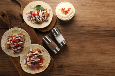 Delicious tacos with vegetables, meat and sauce on wooden table, flat lay. Space for text