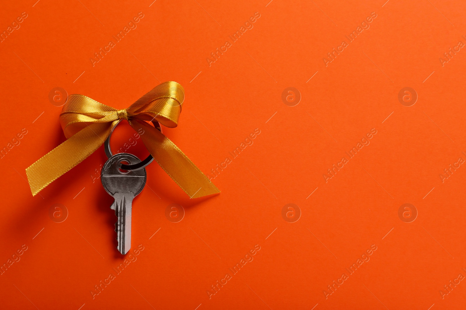 Photo of Key with yellow bow on orange background, top view. Space for text. Housewarming party