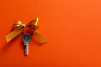 Key with yellow bow on orange background, top view. Space for text. Housewarming party