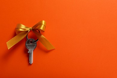 Photo of Key with yellow bow on orange background, top view. Space for text. Housewarming party