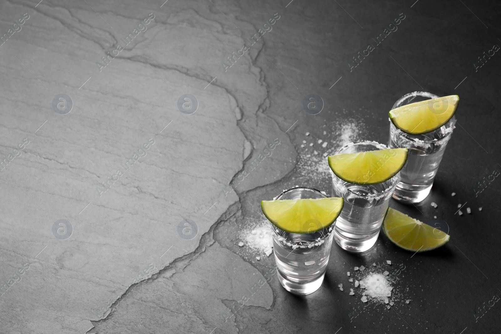 Photo of Mexican Tequila shots, lime slices and salt on black table. Space for text