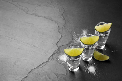 Photo of Mexican Tequila shots, lime slices and salt on black table. Space for text