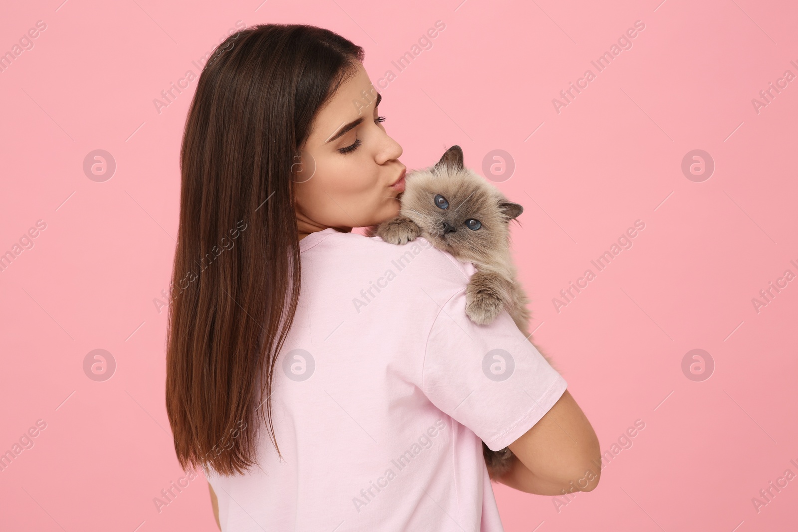 Photo of Woman kissing her cute cat on pink background