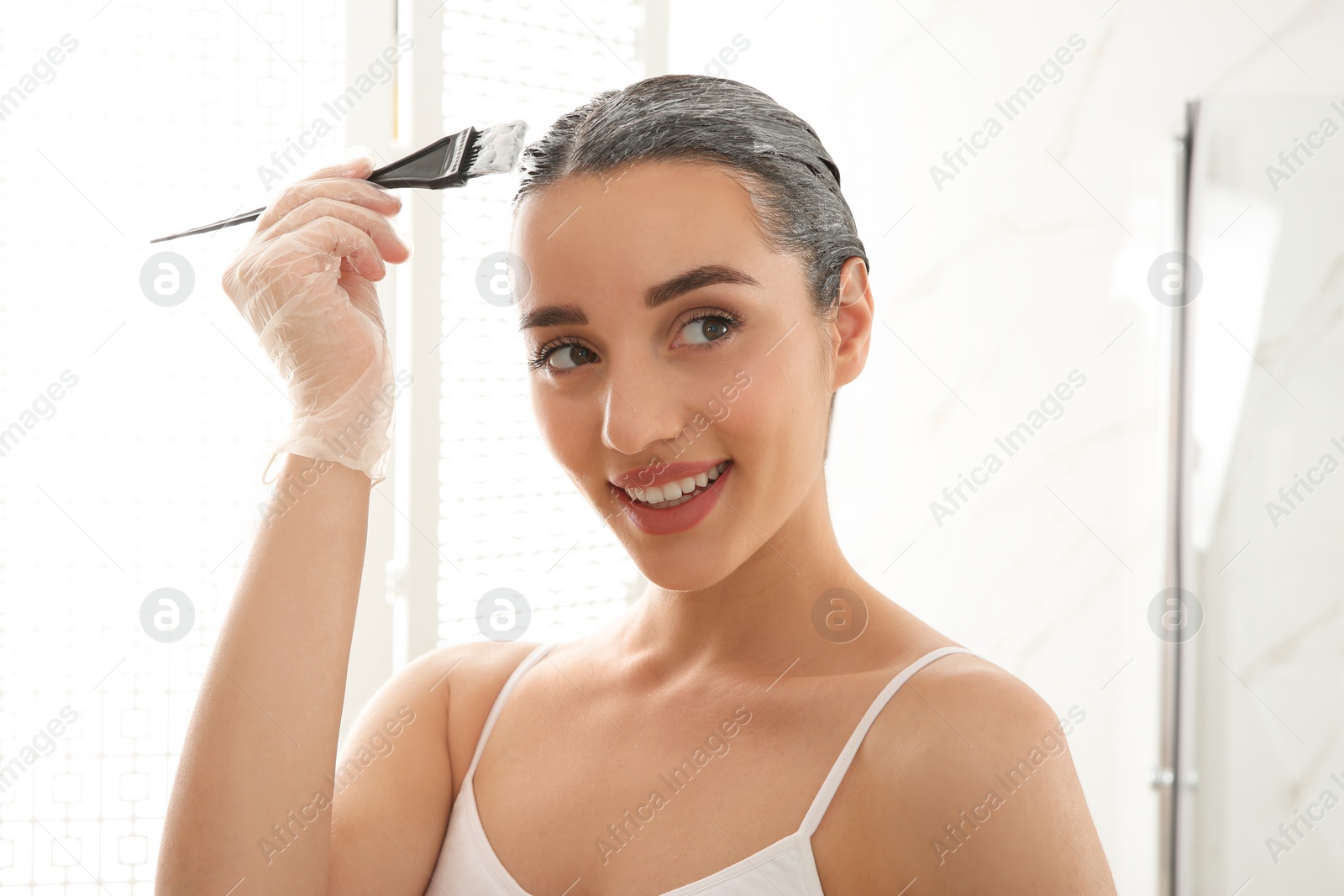 Photo of Young woman dyeing her hair at home