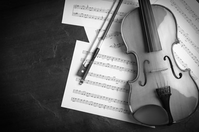 Image of Violin, bow and note sheets on stone table, flat lay. Black and white tone