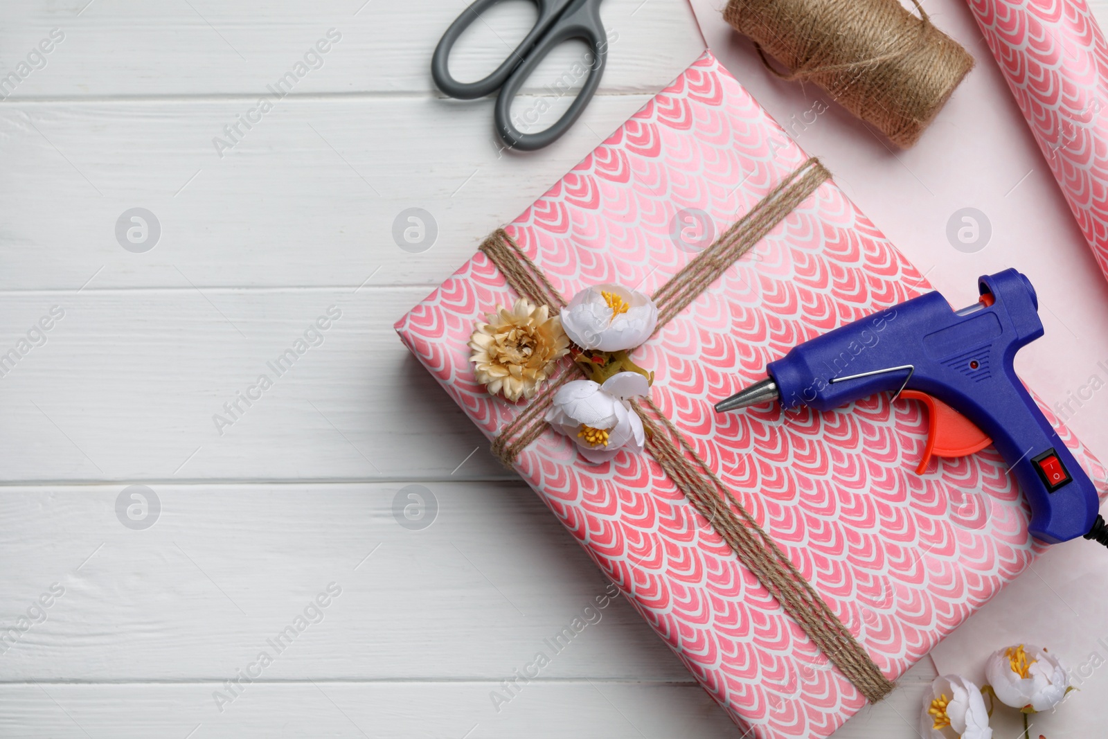 Photo of Flat lay composition with hot glue gun and gift on white wooden table. Space for text