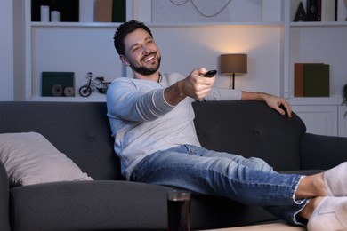 Happy man changing TV channels with remote control on sofa at home