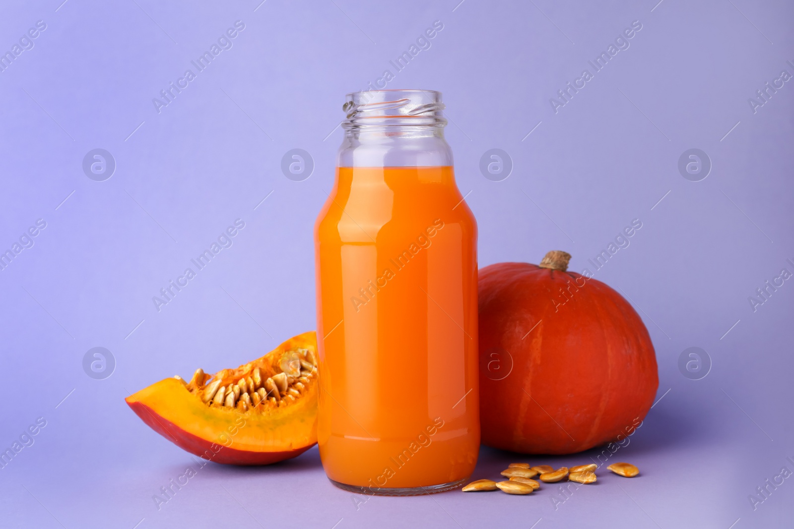 Photo of Tasty pumpkin juice in glass bottle, whole and cut pumpkins on lavender color background