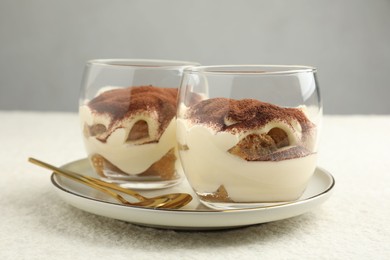 Delicious tiramisu in glasses and spoons on white table, closeup