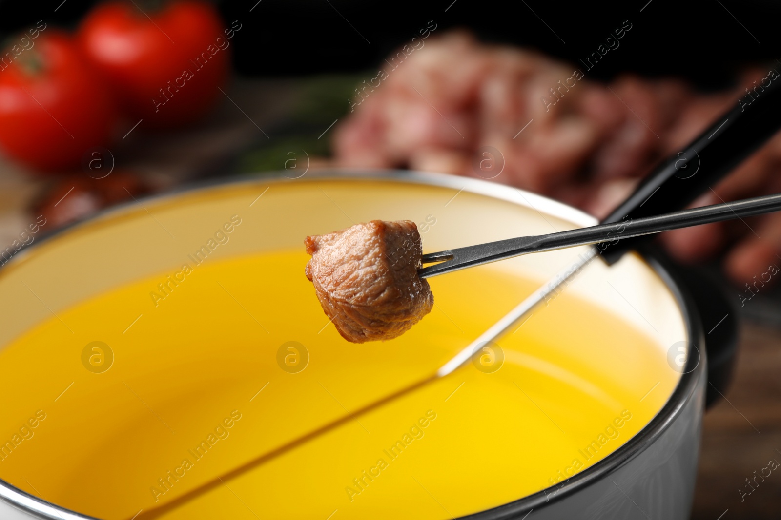 Photo of Fried piece of meat on fondue fork above pot with oil, closeup