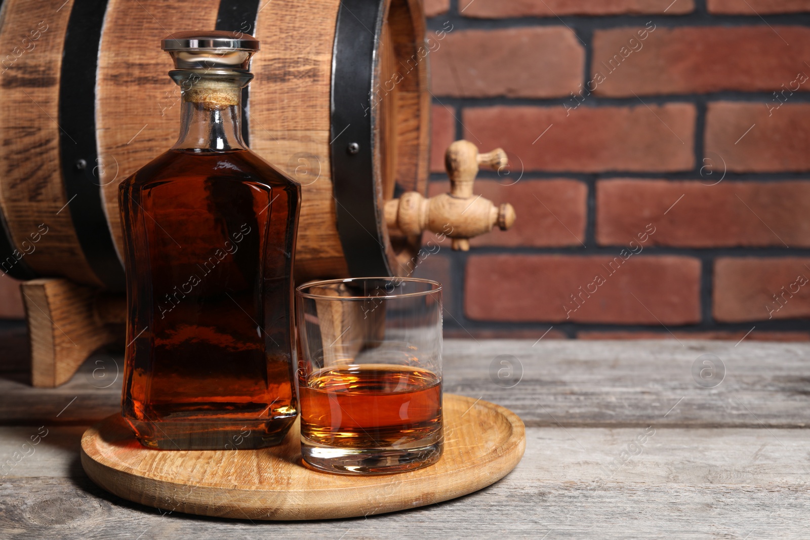Photo of Golden whiskey and barrel on wooden table against brick wall, space for text