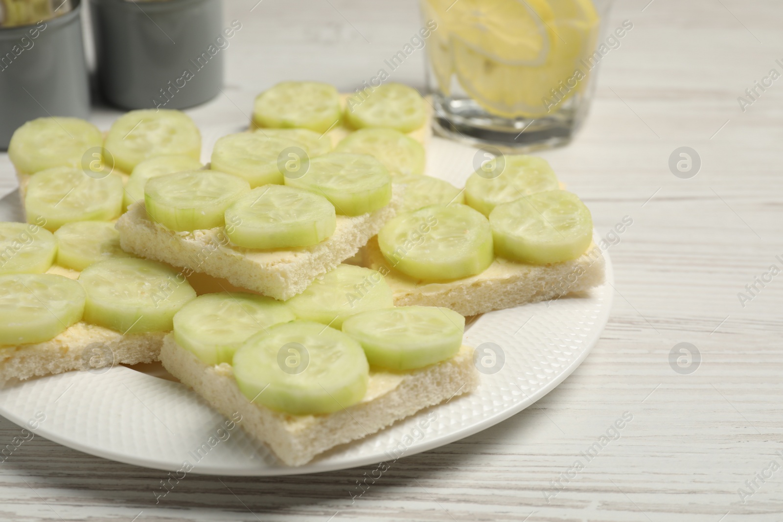 Photo of Tasty sandwiches with butter and cucumber served on white wooden table