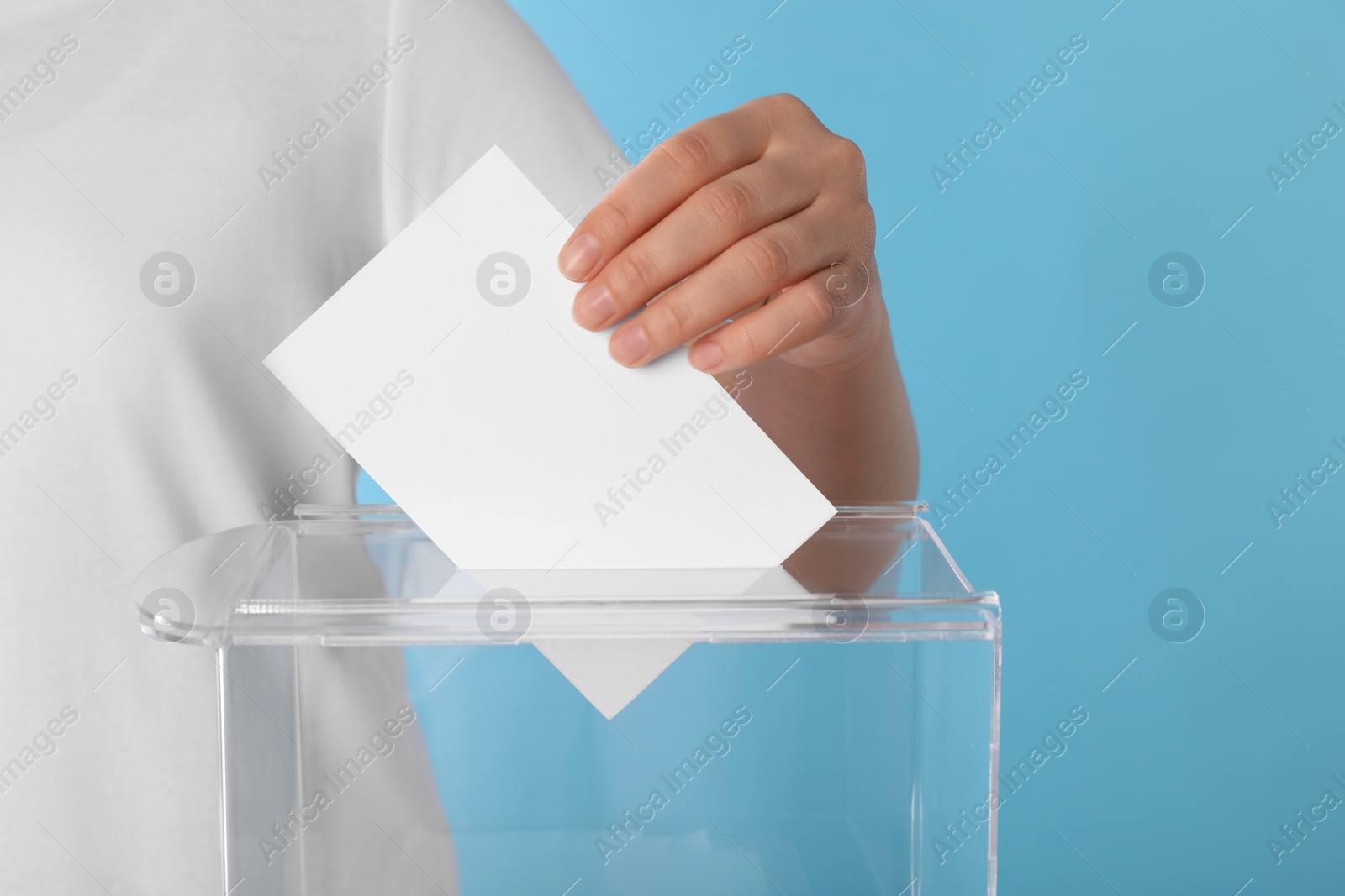 Photo of Woman putting her vote into ballot box on light blue background, closeup