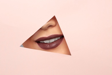 Lips of beautiful young woman with dark lipstick visible through hole in color paper