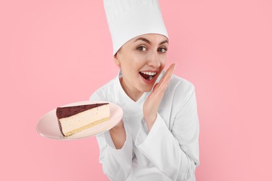 Photo of Happy professional confectioner in uniform holding delicious cheesecake on pink background