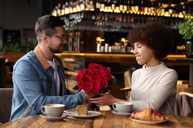 Photo of International dating. Handsome man presenting roses to his girlfriend in cafe