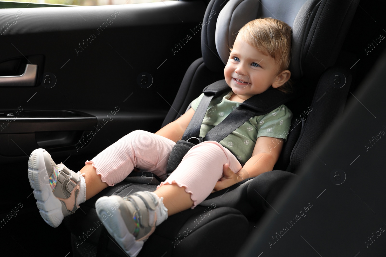 Photo of Cute little girl sitting in child safety seat inside car