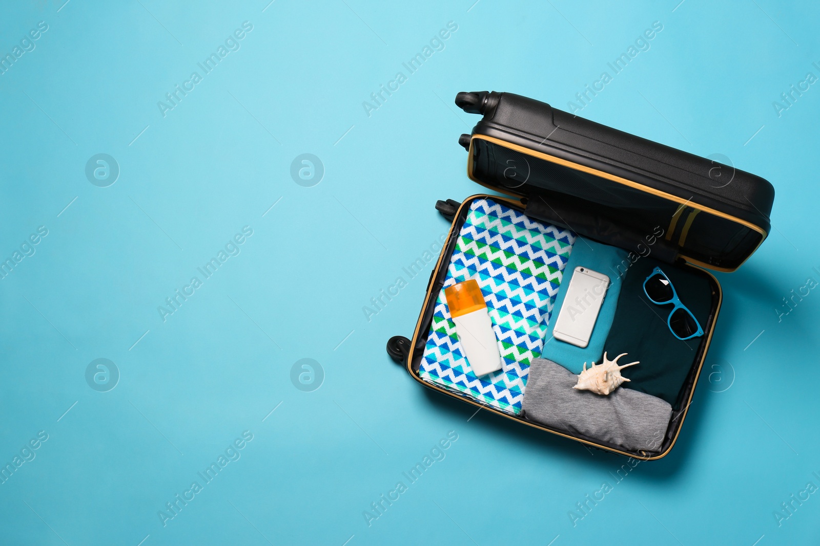 Photo of Open suitcase with traveler's belongings on color background, top view. Space for text