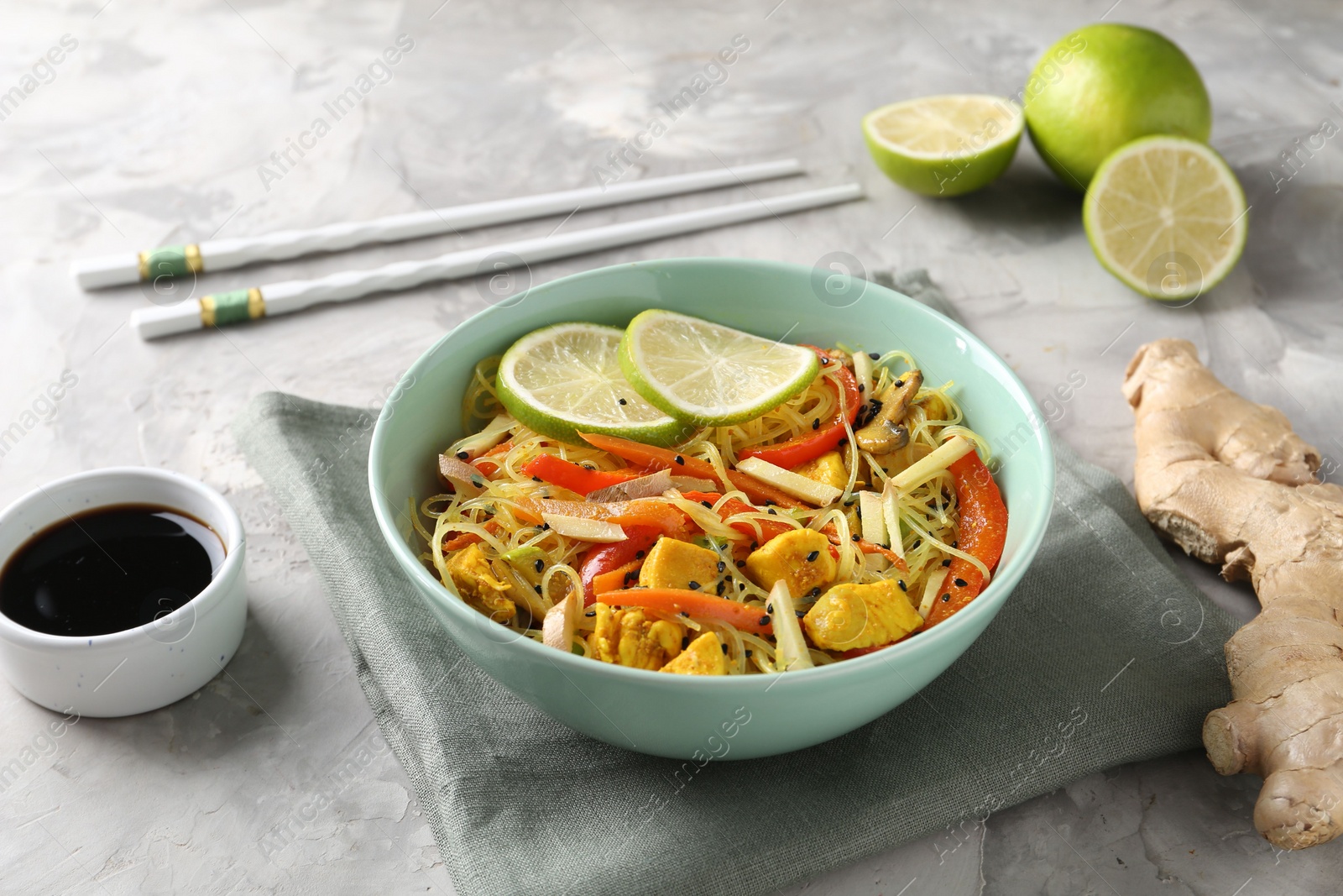 Photo of Stir-fry. Delicious cooked noodles with chicken and vegetables in bowl served on gray textured table