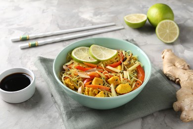 Photo of Stir-fry. Delicious cooked noodles with chicken and vegetables in bowl served on gray textured table