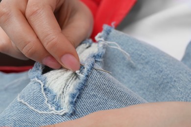 Photo of Woman sewing jeans with needle, closeup view