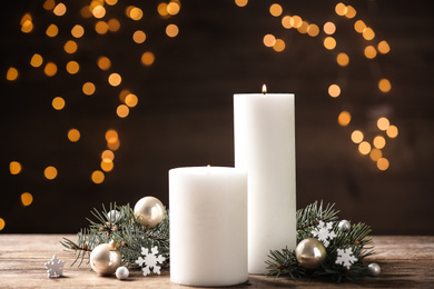 Photo of Candles and Christmas decor on wooden table against blurred festive lights. Winter holiday