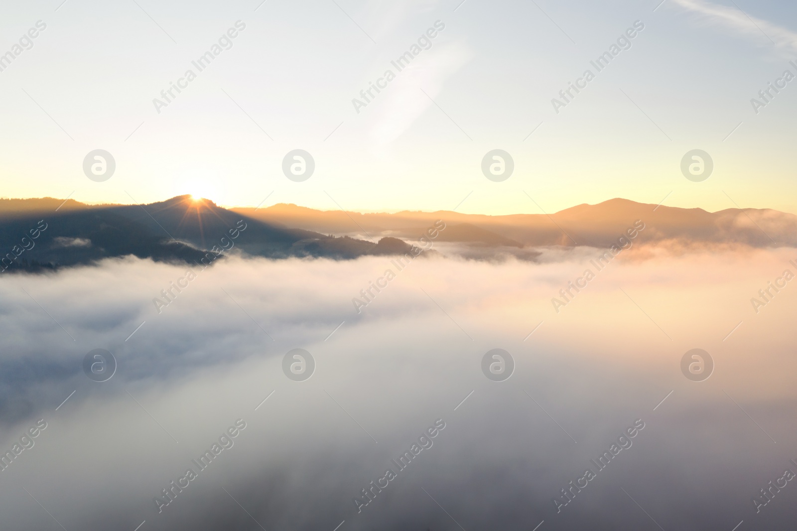 Image of Aerial view of beautiful mountains covered with fluffy clouds at sunrise. Drone photography
