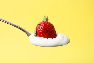 Photo of Spoon with yogurt and strawberry on yellow background, closeup