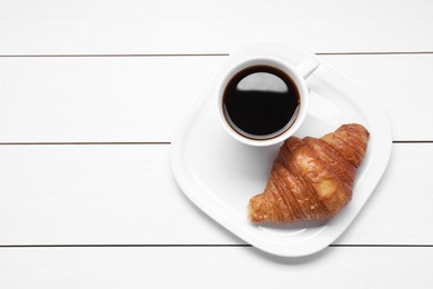 Photo of Tasty breakfast. Cup of coffee and croissant on white wooden table, top view. Space for text