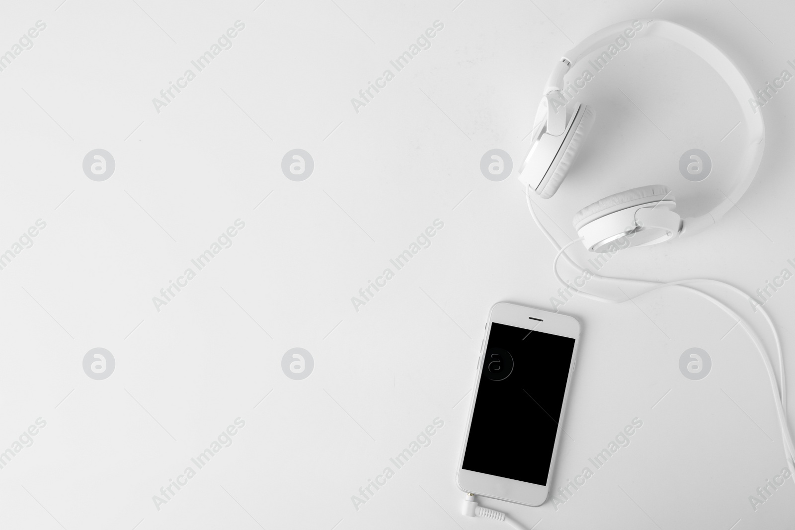 Photo of Smartphone with headphones on white background, top view. Space for text